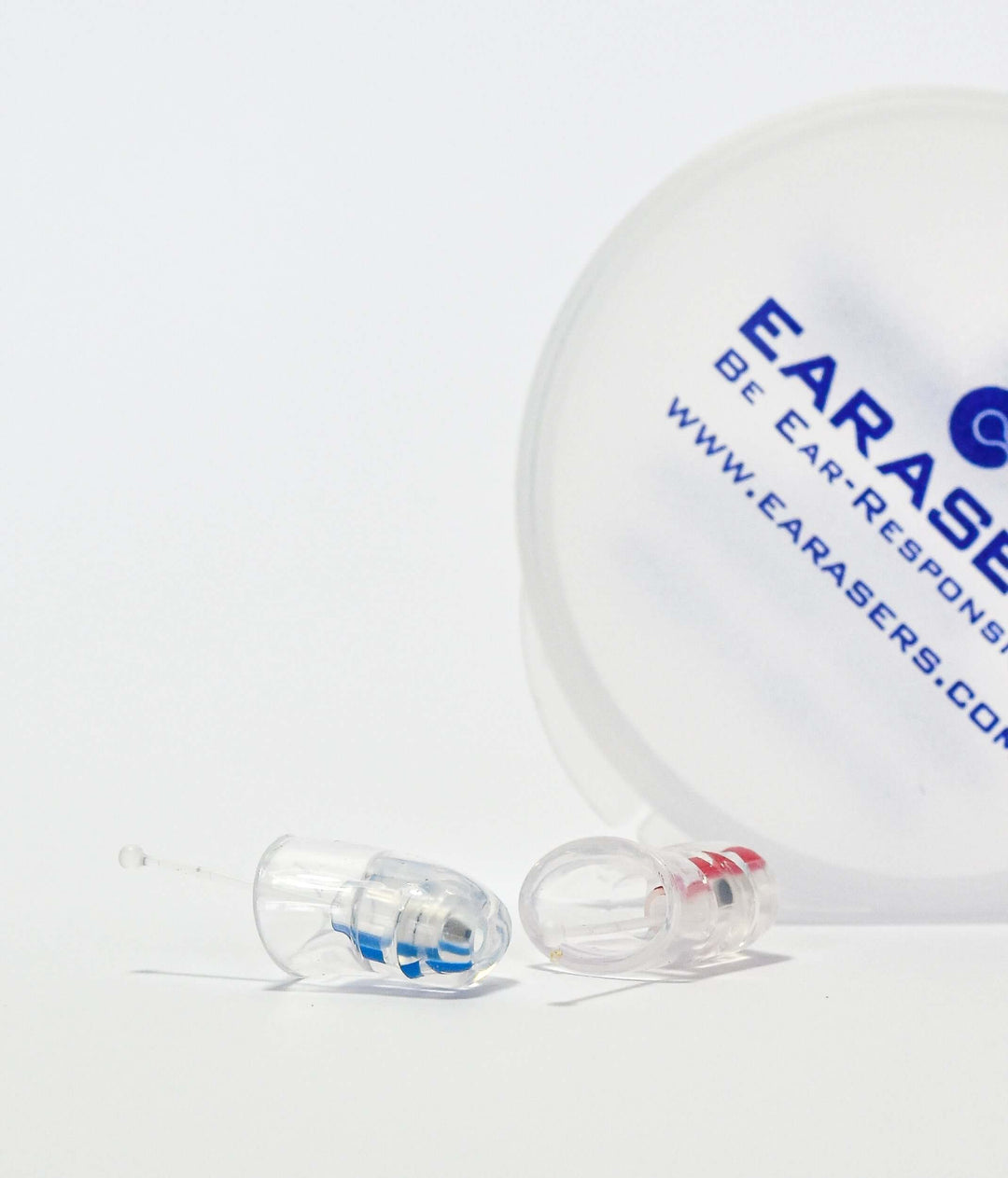 Two clear earplugs with blue and red accents resting on a white surface, with a translucent white round container in the background printed with the brand name EARASErs.