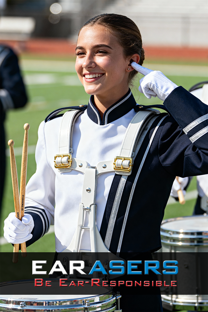 Person in marching band uniform with drum, wearing ear protectors, on a sports field.