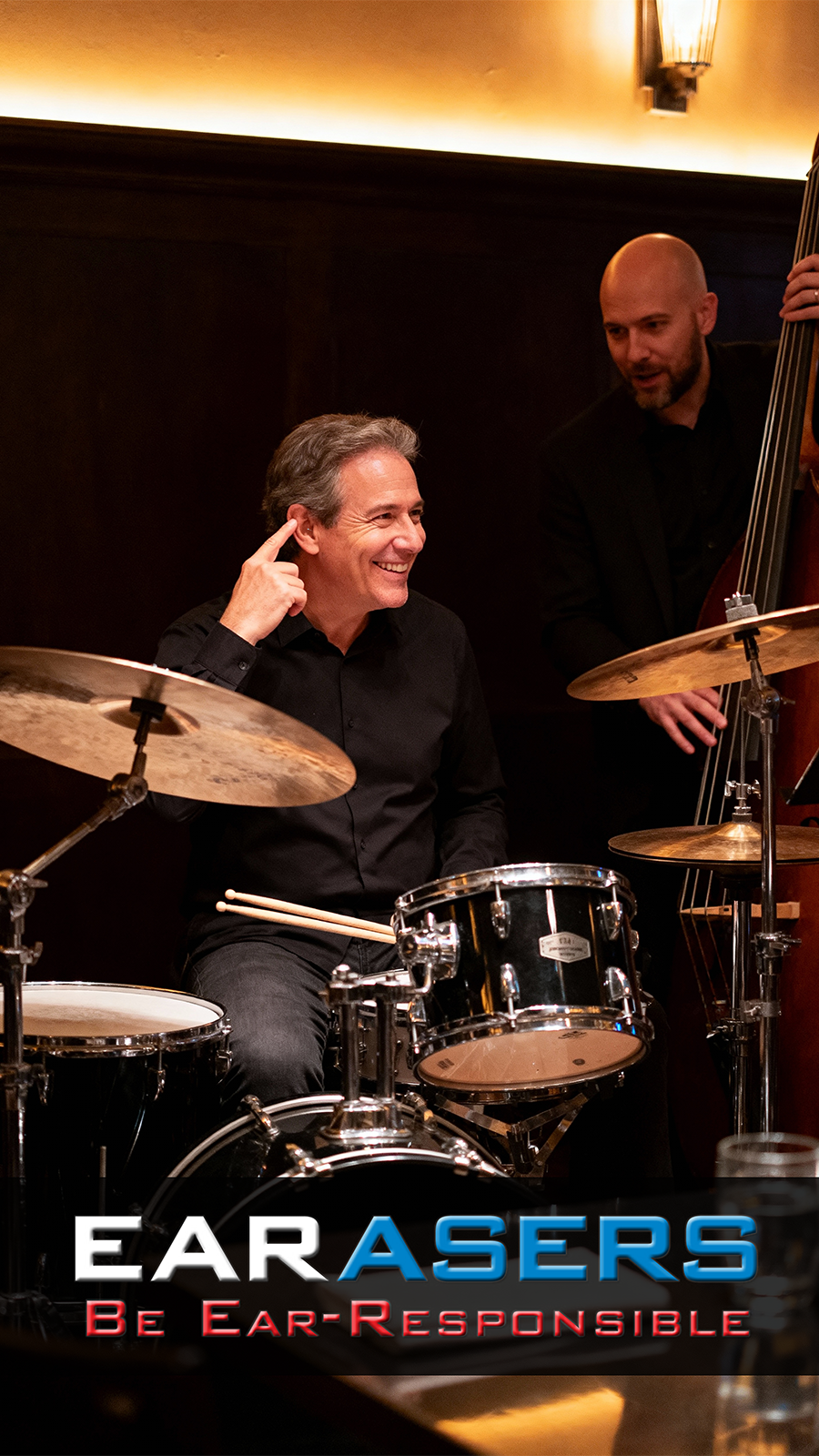 drummer at drumset pointing at ear wearing earasers