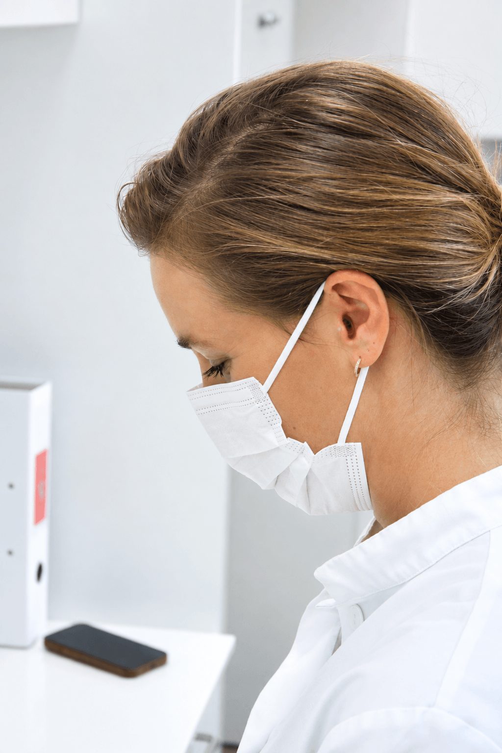 left side profile of a woman in a surgical mask looking down. there is an earplug in her ear.