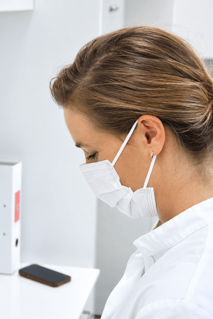 left side profile of a woman in a surgical mask looking down. there is an earplug in her ear.