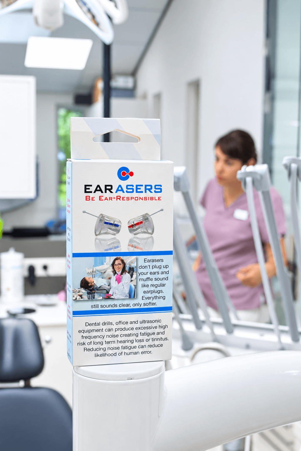 Earasers box sits on top of a dental workstation in a dentist's office with a dental hygienist in the background