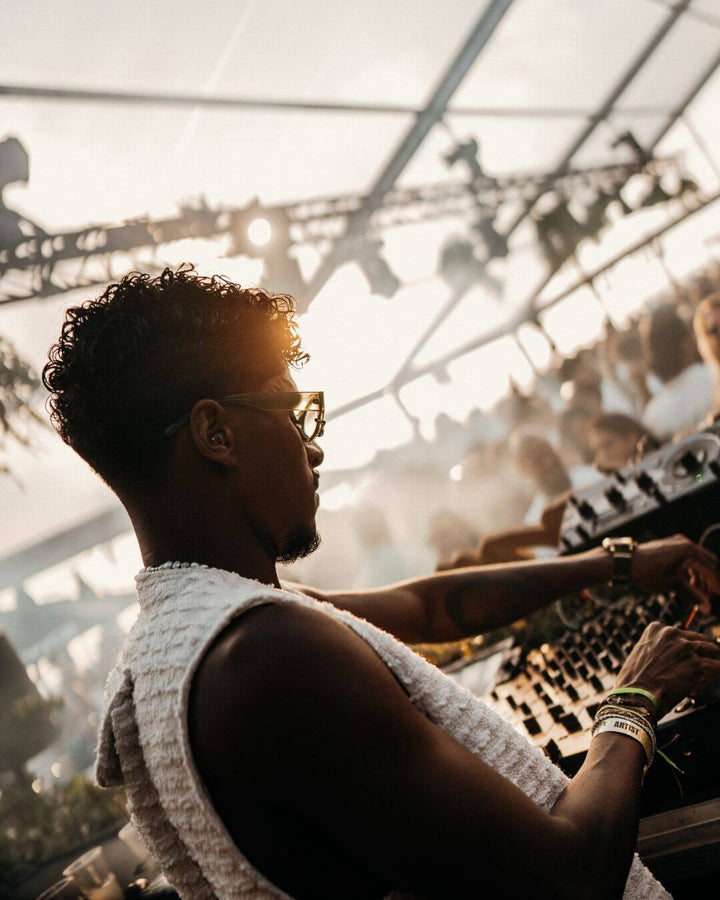 right side profile of a dj mixing music in front of a crowd with an earplug in his ear