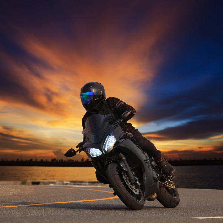 A rider in full black gear on a sport motorcycle, with a sunset behind them